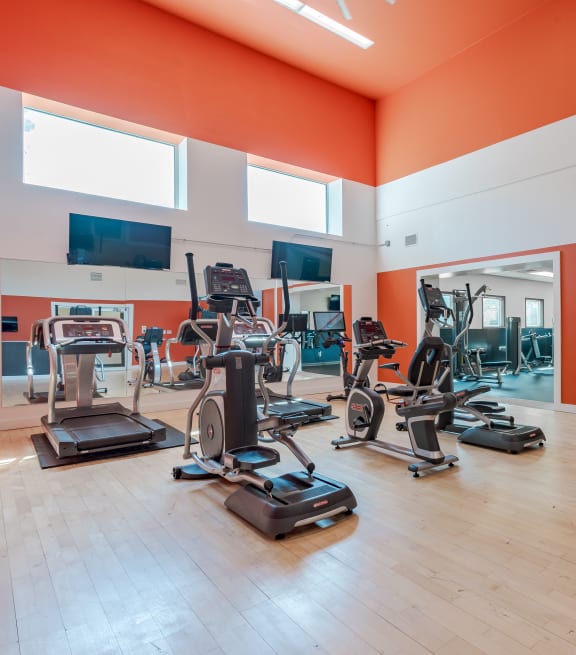 a gym with weights and cardio equipment in a building with orange walls
