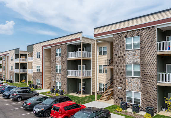 an exterior view of an apartment building with cars parked in a parking lot