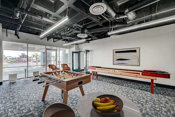 A room with a foosball table, a bench, and a bowl of fruit on a table.