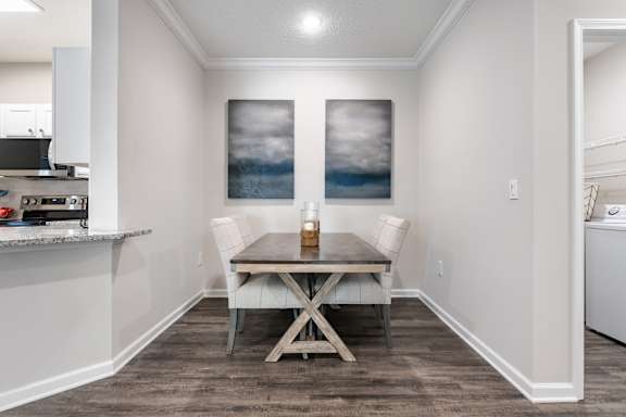 A dining room with a table and chairs and a painting on the wall.