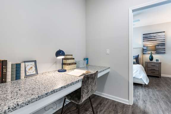 A room with a desk, chair, and a bed in the background.