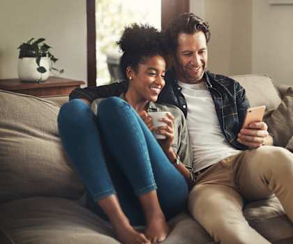 a man and woman sitting on a couch looking at a cell phone