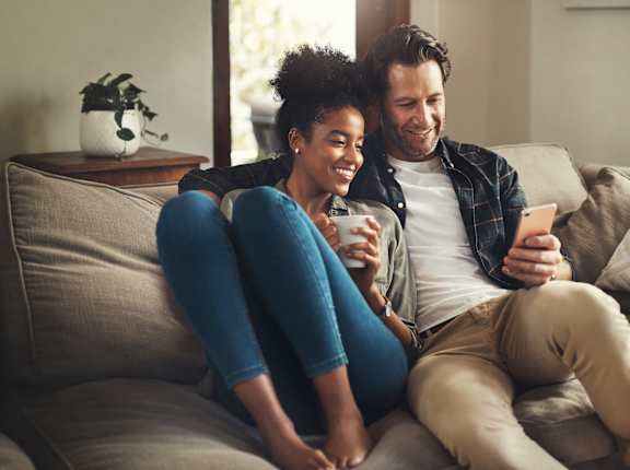 a man and woman sitting on a couch looking at a cell phone