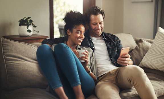 a man and woman sitting on a couch looking at a cell phone