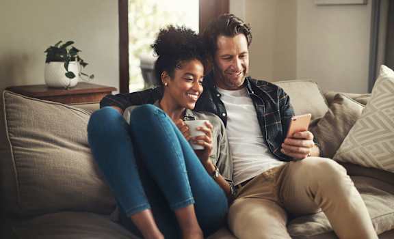 a man and woman sitting on a couch looking at a cell phone