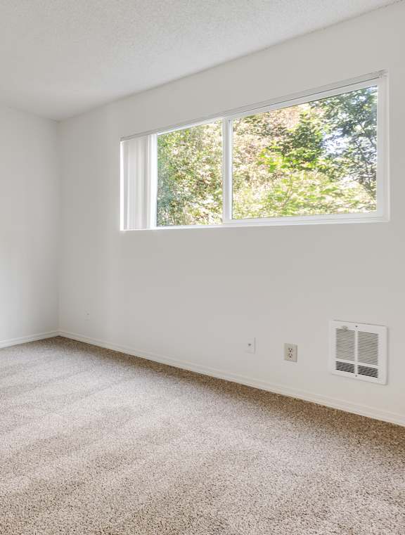 A room with a ceiling fan and a window overlooking trees.