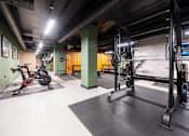 Thumbnail 7 of 8 - A gym with a variety of equipment including a stationary bike and a squat rack.