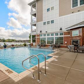 A pool with a wooden deck and lounge chairs in front of a building.