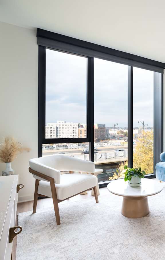 A blue couch sits in a living room with a large window overlooking the city.