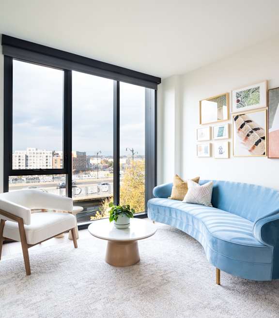 A blue couch sits in a living room with a large window overlooking the city.