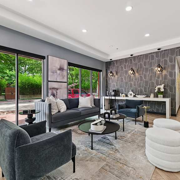 A modern living room with a grey sofa, a black coffee table, a grey armchair, a white pouf, and a grey rug.