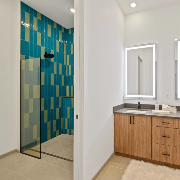 A bathroom with a blue tiled shower and a double sink vanity at Four23/Hoge, Cincinnati, 45226.