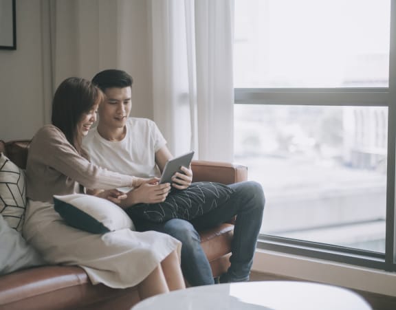 a young woman and man sitting on couch looking at tablet at Topaz Apartments, Los Angeles, California