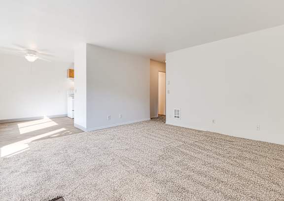 A large, empty room with a carpeted floor and a ceiling fan.
