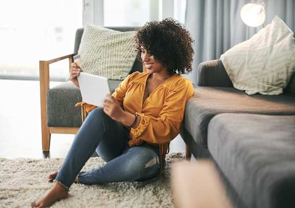 A woman in a yellow top and blue jeans is sitting on the floor in a living room.