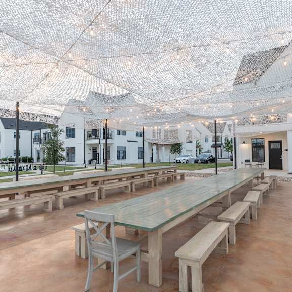 A large outdoor dining area with tables and benches under a net of lights.