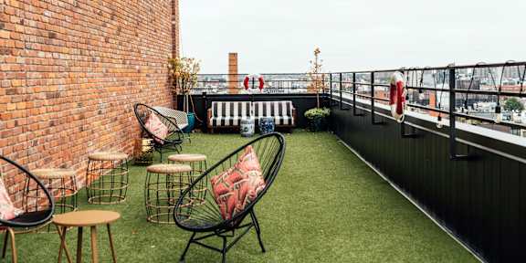 A balcony with a black railing, a brick wall, and a green lawn with chairs and a table.