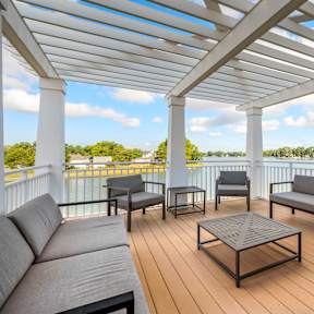 A white pergola over a wooden deck with grey couches and a coffee table.