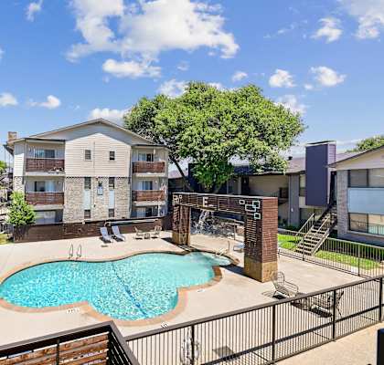 A pool surrounded by a fence and chairs in front of a building.