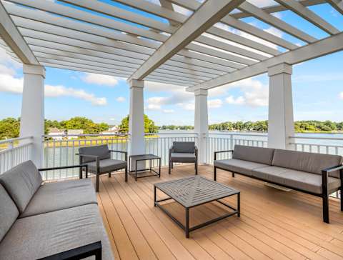 A white pergola with blue chairs and plants on a deck overlooking a body of water. at River House Apartments, Norfolk, VA