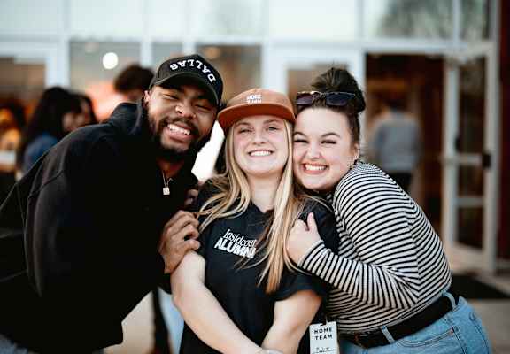 Three people hug each other in front of a glass door.