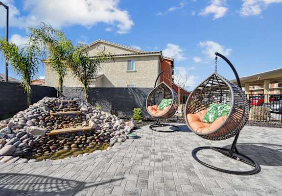 A patio with two hanging chairs and a fire pit.