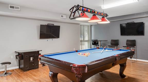 A pool table is in the middle of a room with a TV and a chair.