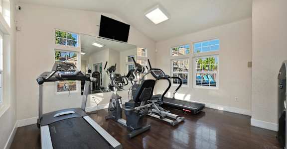 the gym has plenty of exercise equipment and a flat screen tv at Hidden Oaks Apartments, Citrus Heights, CA