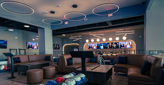 A bowling alley with a row of balls and chairs.