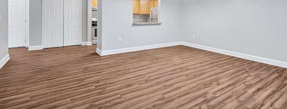 an empty living room with wood flooring and a kitchen