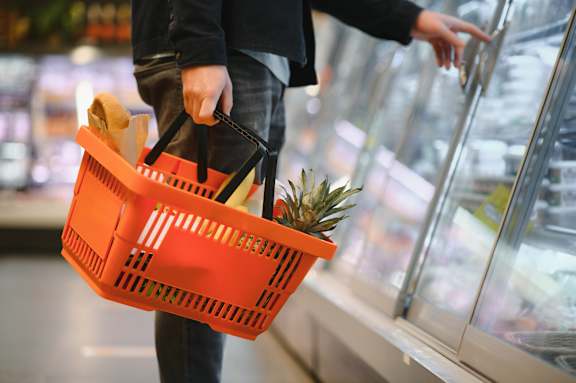 A person holding an orange shopping basket with a pineapple in it.