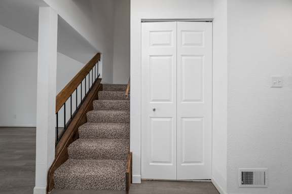 a view of the stairway from the entryway with a white door and carpeted stairs