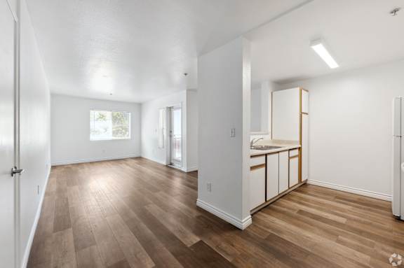 an empty living room and kitchen with wood flooring and white walls
