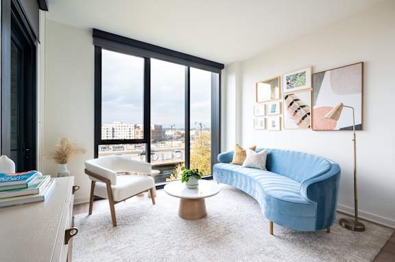 A blue couch sits in a living room with a large window overlooking the city.