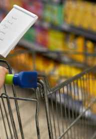 A person is checking off items on a list while pushing a shopping cart.