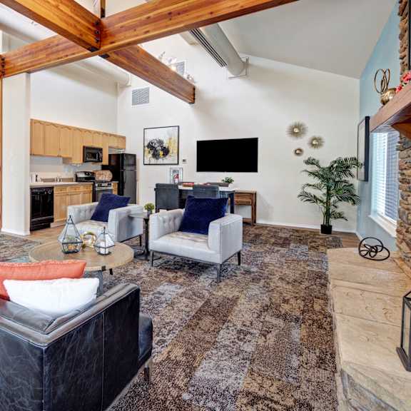 The amazing resident lounge with black couches, a fireplace, decorations, large windows, unique overhead lighting, wooden beam ceiling, white plush chairs, and coffee tables at and a community kitchen with a coffee station, refrigerator, and TV at the Highlands Luxury Residences. 