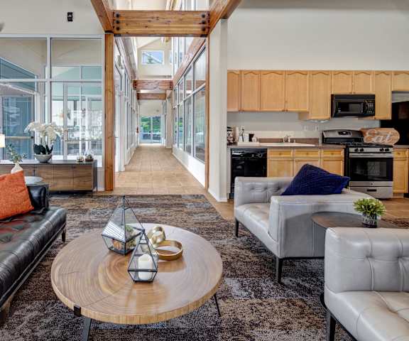 The amazing resident lounge with black couches, a fireplace, decorations, large windows, unique overhead lighting, wooden beam ceiling, white plush chairs, and coffee tables at and a community kitchen with a coffee station, refrigerator, and TV at the Highlands Luxury Residences. 