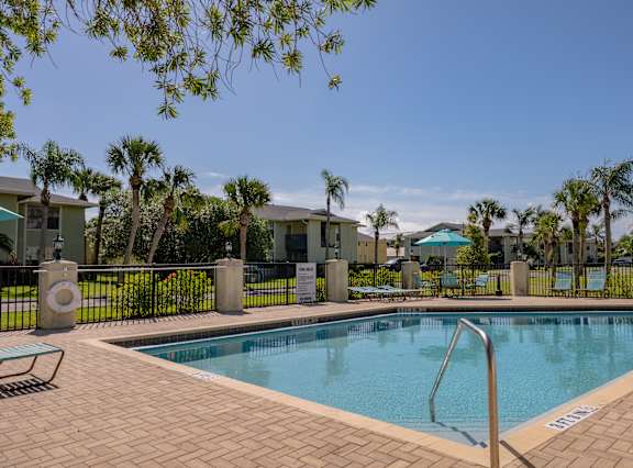 A swimming pool surrounded by a brick patio and palm trees.