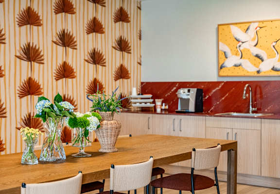 A kitchen with a wooden table and chairs, a sink, and a painting on the wall.