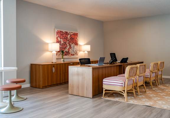 A room with a desk, chairs, and a painting on the wall.