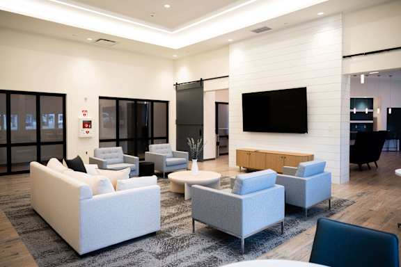 A modern living room with white furniture and a flat screen TV mounted on the wall.