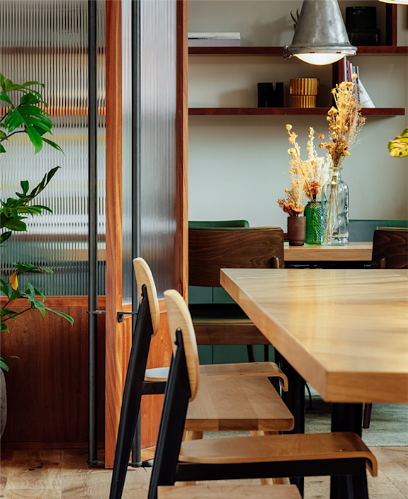 a wooden table in a restaurant with chairs and a plant