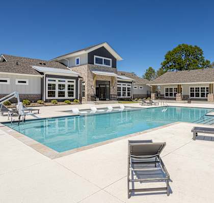 A large swimming pool with lounge chairs and a house in the background.