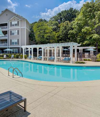 A swimming pool surrounded by sun loungers and umbrellas in front of apartment buildings.