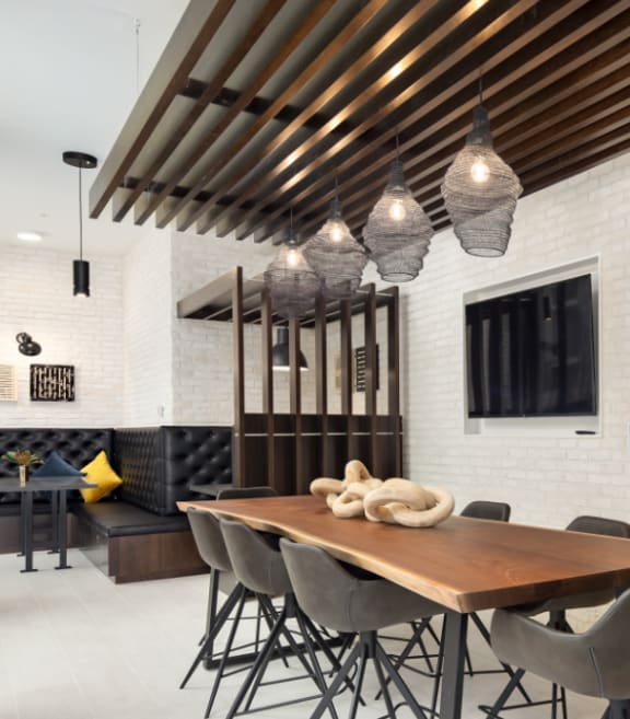 a long wooden table with black chairs in a room with white brick walls and a large tv