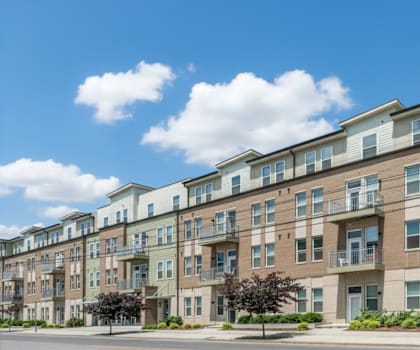 A row of modern apartment buildings with balconies and trees in front.