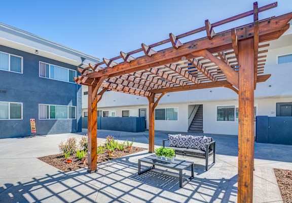 A wooden pergola is over a table in a courtyard.