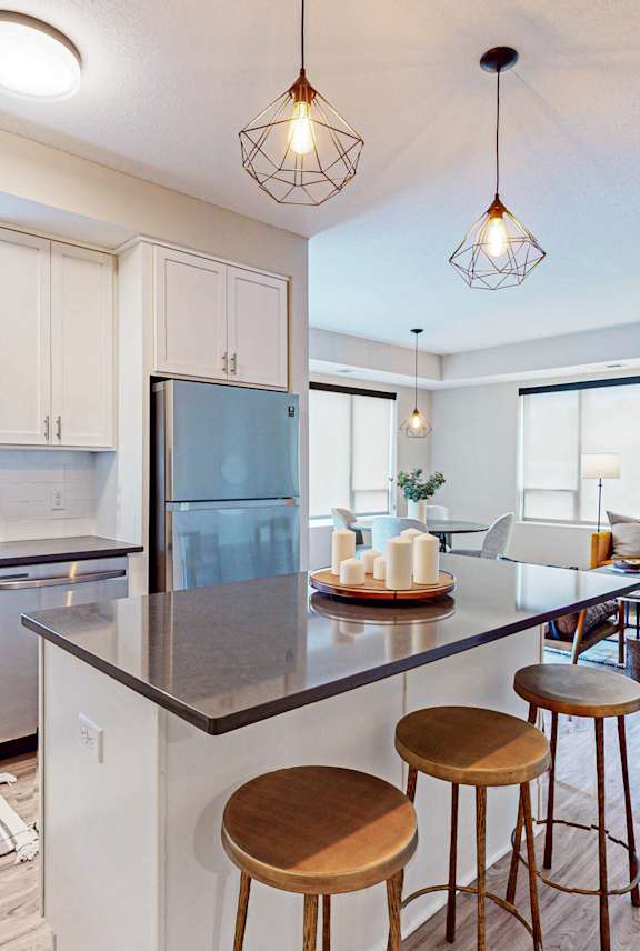 A kitchen with white cabinets and a black countertop with a refrigerator, sink, and bar stools.