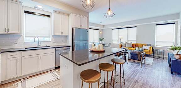 A kitchen with white cabinets and a black countertop with a refrigerator, sink, and bar stools.