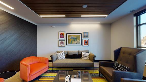 A living room with a grey couch, orange armchair, and a coffee table at The Bessemer at Seward Commons Apartments, Minneapolis, 55404
